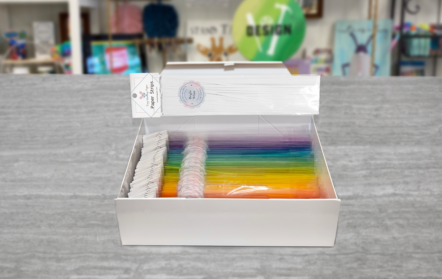 A white box with the text 'Easy Quilling Paper' on the top and 'Masterpiece Box 50 colors + bag stand + travel box' on the bottom. The box is open and filled with colorful quilling paper strips.